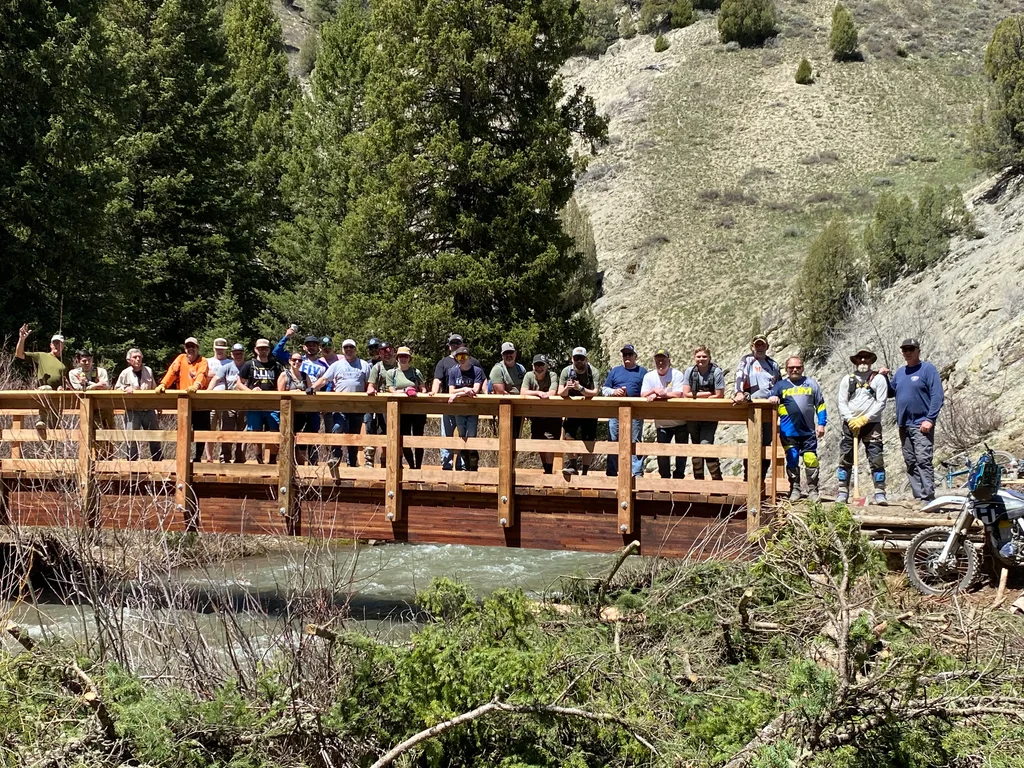 Dozens of volunteers lined up along the railing of a new wooden bridge over a creek.