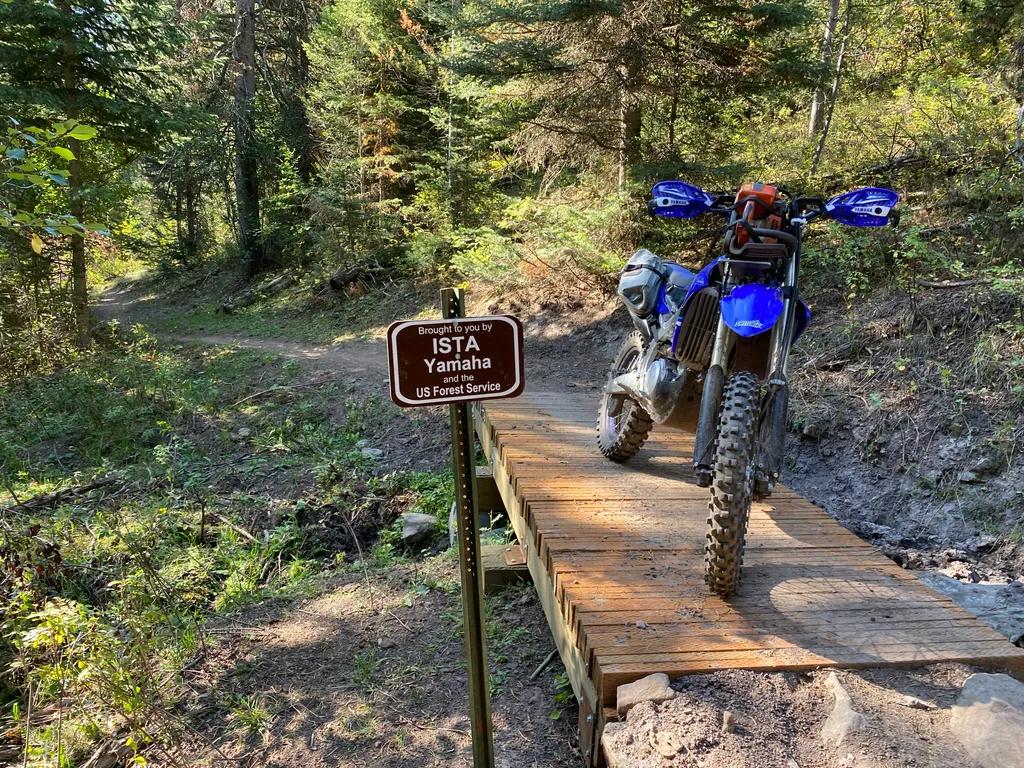 A motorcycle on a wooden trail bridge, beside a sign: Brought to you by ISTA, Yamaha and the US Forest Service.