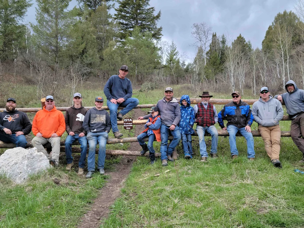 Volunteers and their kids sitting along a new log fence beside the trail.