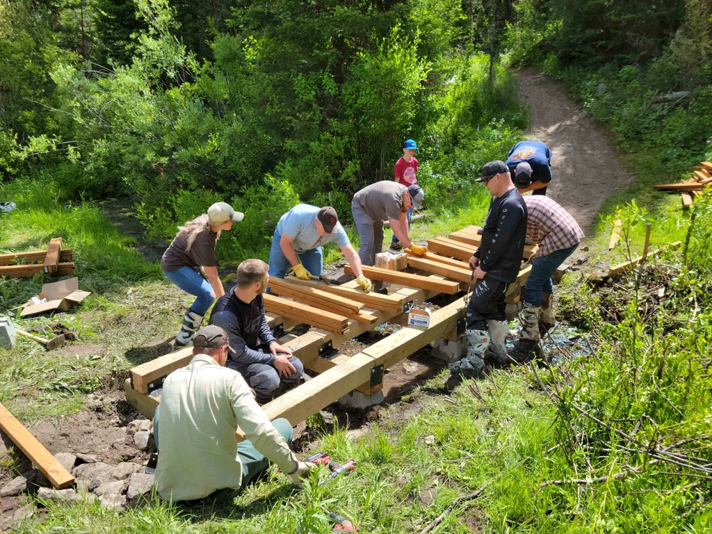 Volunteers fastening timbers to build a small bridge where the trail crosses a stream.
