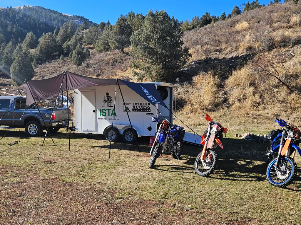 The ISTA trailer parked at a trailhead with three dirt bikes beside it.